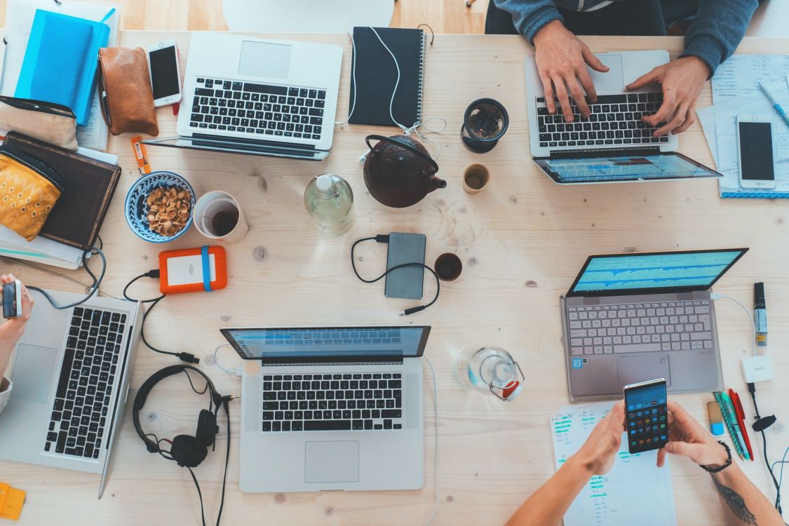 Eine Gruppe Menschen, die um einen Tisch herum sitzen und alle an ihren Laptops arbeiten