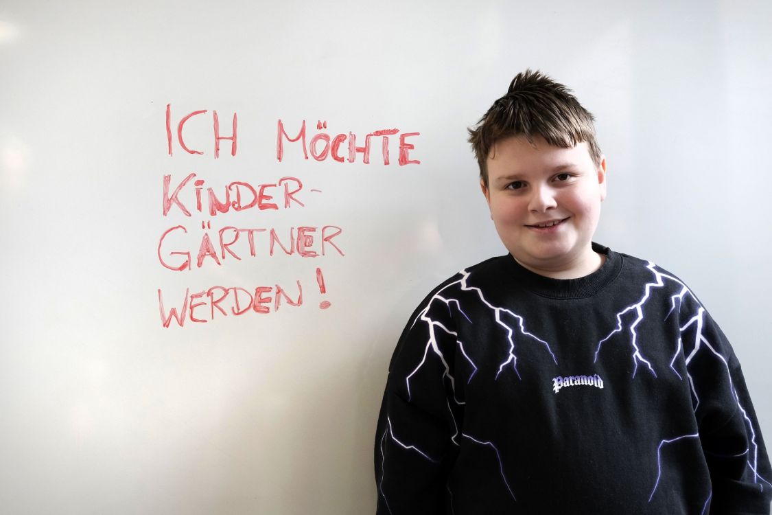 Kind vor einer Tafel, auf der geschrieben steht "Ich will Kindergärtner werden."