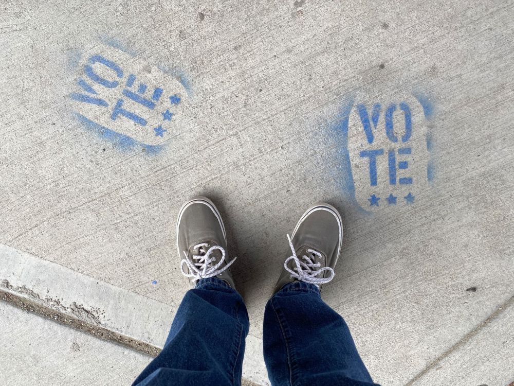 Person in Jeans und Sneakers steht zwischen zwei blauen Schriftzügen mit dem Wort