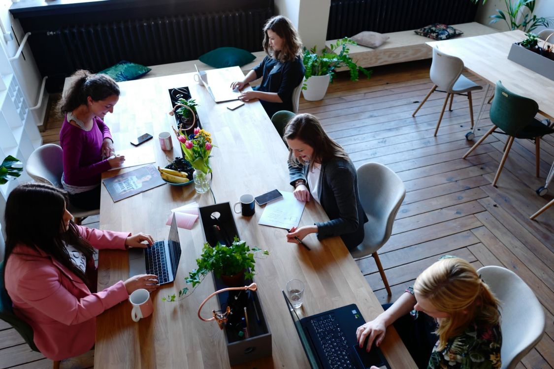 F&uuml;nf Frauen sitzen an einem gro&szlig;en Tisch und arbeiten