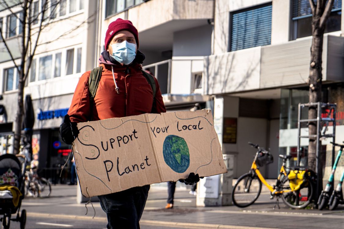Junger Mann mit einem Schild in der Hand, auf dem steht "Support your local planet".