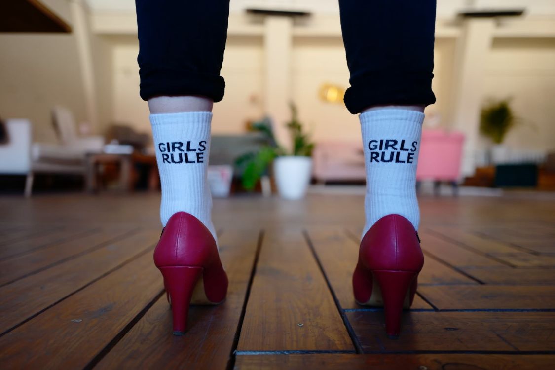 Person in roten High Heels und Socken, die Aufschrift auf den Socken lautet: 