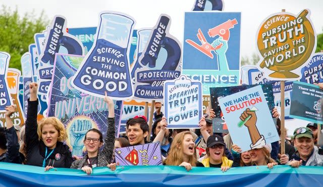Demonstration von Wissenschaftler*innen. Demonstrant*innen halten Plakate hoch mit der Aufschrift "Science serving the common good" oder "We have the solution".