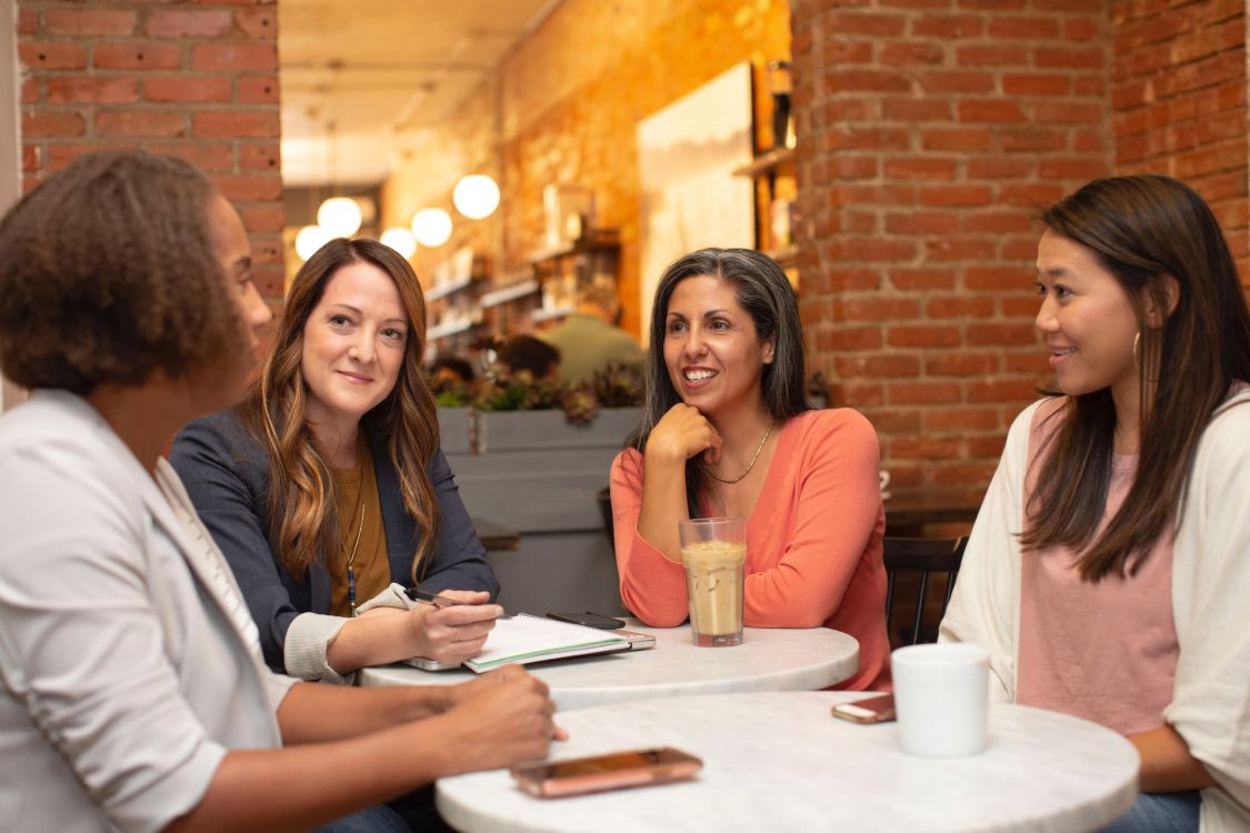 Vier Frauen sitzen zusammen in einem Café und unterhalten sich.