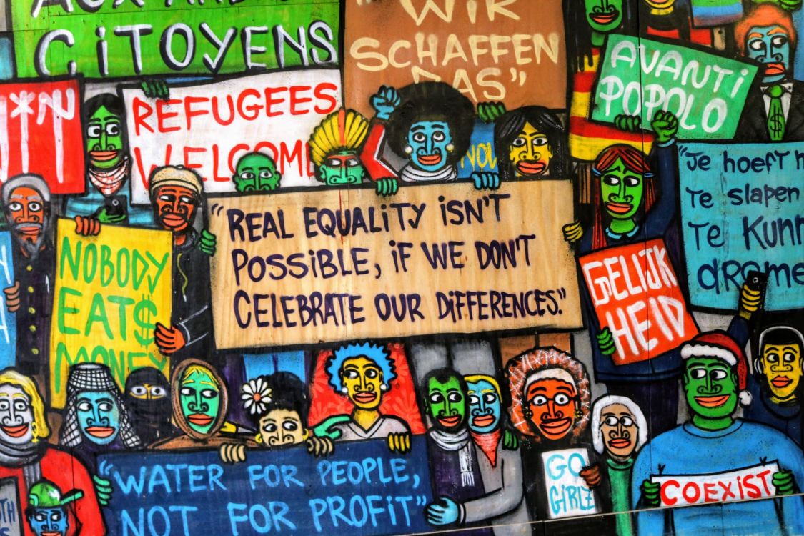 Buntes Wandgraffitti mit den Aufschriften "Refugees welcome" und "Real equalitiy is not possible if we don't celebrate our differences".