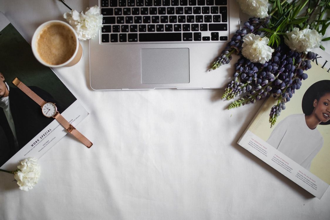 Laptop umringt von Blumen, Zeitschriften und einer Tasse Kaffee