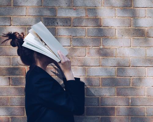 Junge Frau, die ihr Gesicht mit einem Buch verdeckt