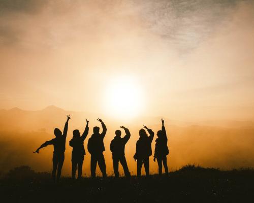 Gruppe sich freuender Menschen von hinten vor Sonnenuntergang