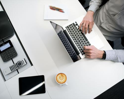 Mann im Hemd am Schreibtisch mit Laptop und Notizblock, Perspektive von oben
