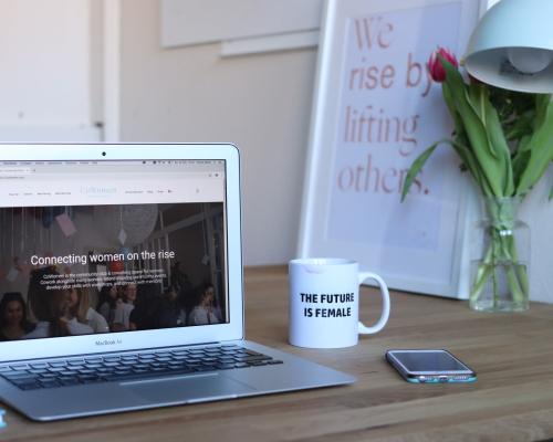 Computer, Kaffeetasse und Handy auf einem Schreibtisch. Auf dem Bildschirm steht: "Connecting women on the rise". Auf der Tasse steht: "THE FUTURE IS FEMALE"