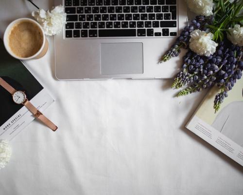 Laptop umringt von Blumen, Zeitschriften und einer Tasse Kaffee